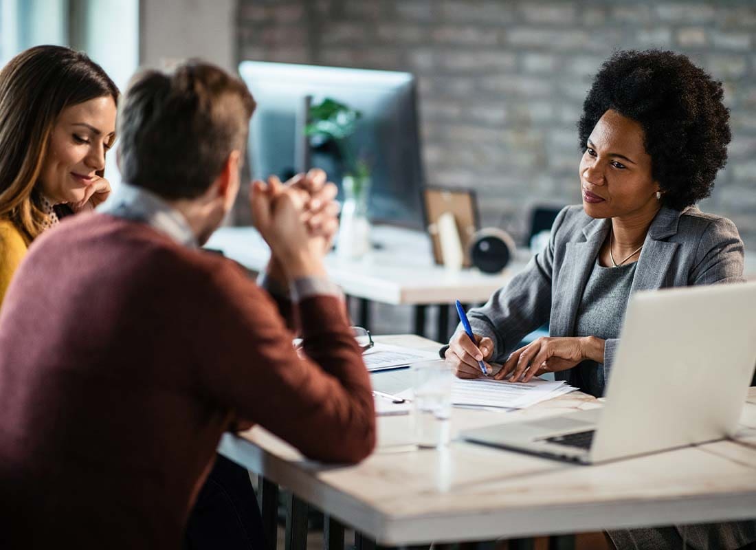 Health Reimbursement Arrangement - Female Insurance Agent Filing a Report on Health Care Reimbursement While Talking to a Couple during a Meeting in a Large Office