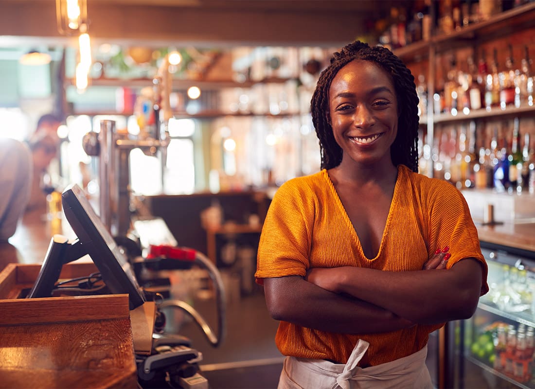 Business Insurance - Portrait Of Smiling Female Bar Owner Standing Behind Counter