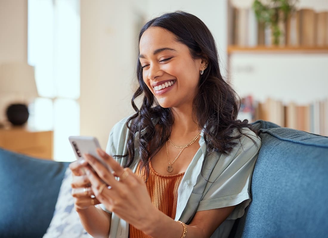 Newsletters - Young Woman Looking at Her Phone While Smiling and Sitting on the Couch